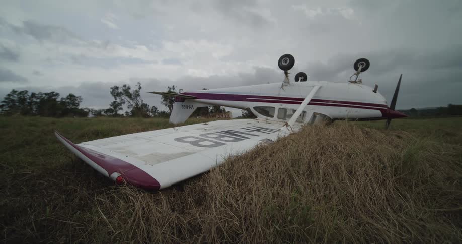 Small airplane lying upside down in a field under a cloudy sky