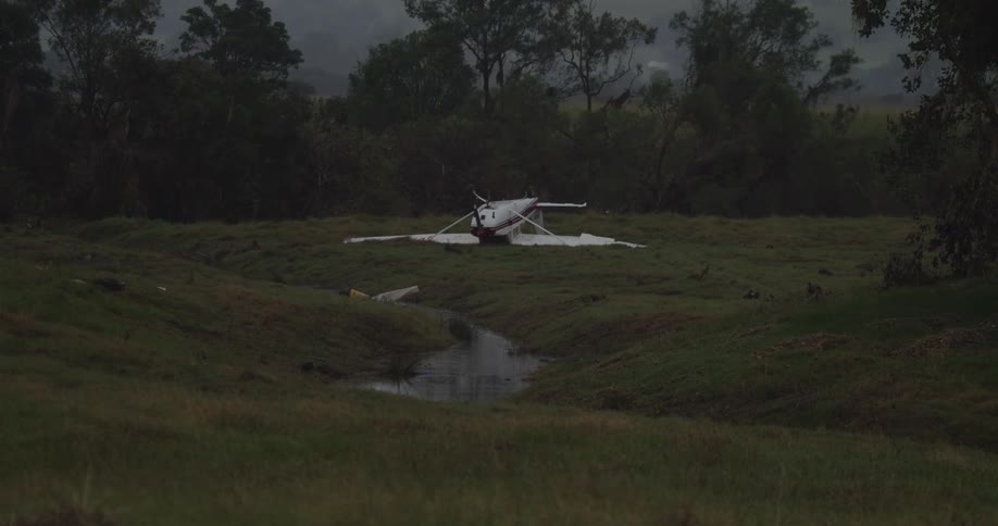 Small airplane lying upside down next to a stream under a dark cloudy sky
