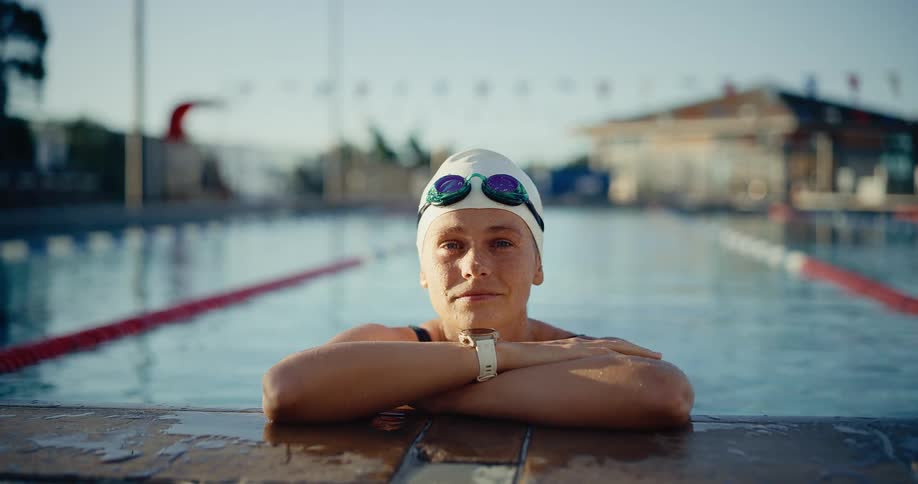Swimmer resting on the edge of a pool wearing a swim cap and goggles