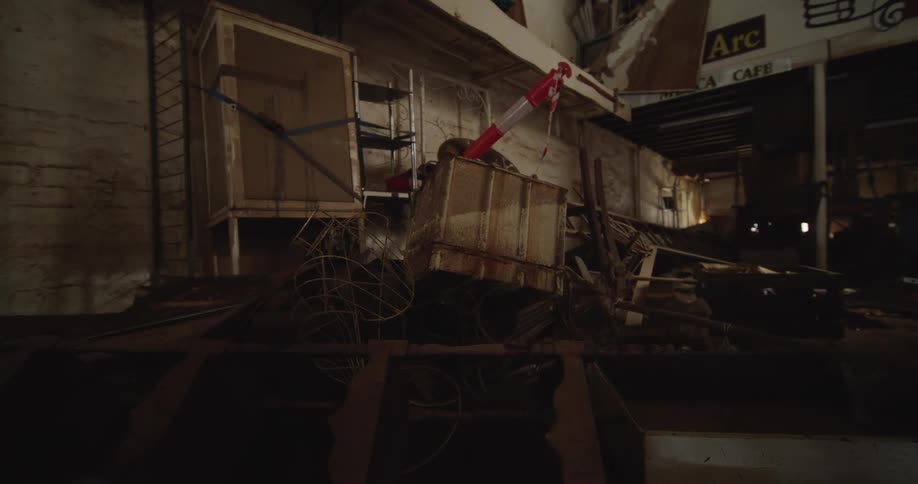 A skip full of debris is being loaded or shifted on the ground of a dimly lit interior demolition site