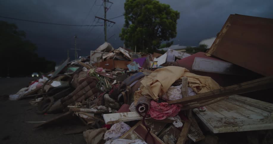 Pile of debris and damaged furniture lines roadside beneath dark and threatening sky