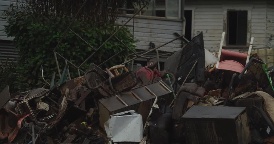 A lot of garbage stacked up outside of a rural house