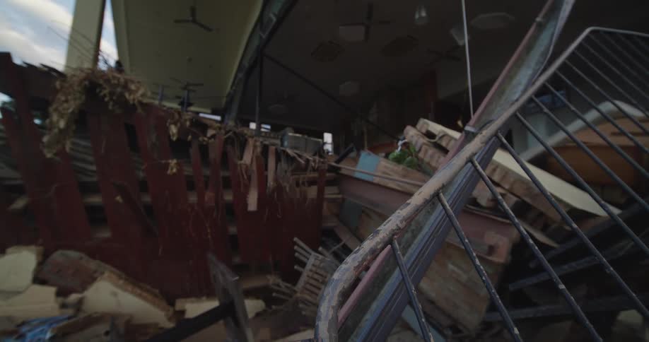 Damaged structure with broken furniture and hanging fans fills interior of ruined building
