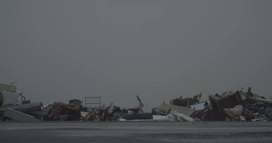 White truck passing on a road next to a massive pile of garbage with broken furniture and many broken objects outdoors