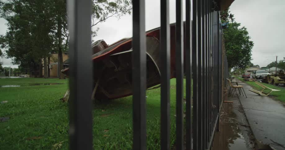 Boat flipped upside down and leaning against a fence in a neighborhood yard