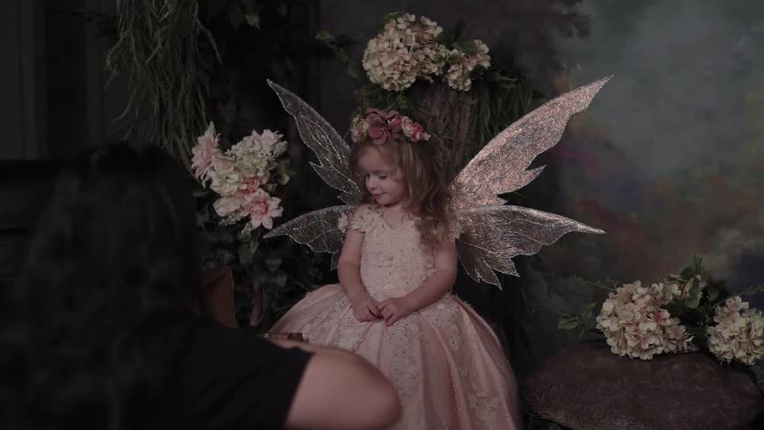 Small girl dressed as a fairy posing on a studio while a young adult woman takes pictures indoors