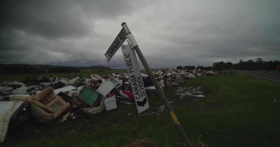 Trash lies on the side of the road near a signpost as cars pass by on a cloudy day