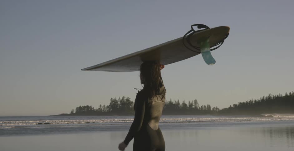 A woman stands on the beach holding a surfboard on her head