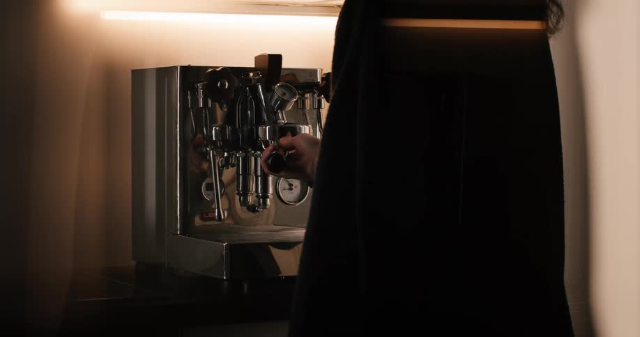 A person adds ground coffee into a coffee maker with light beaming on top of it