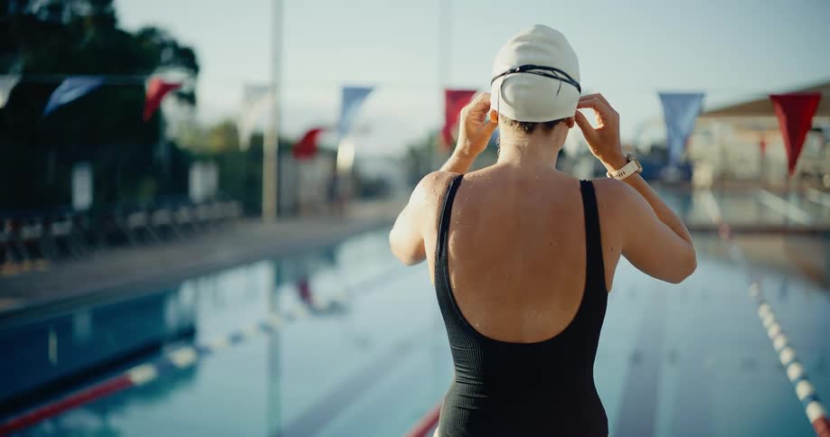 Swimmer with white cap adjusting goggles at outdoor pool edge under clear sky