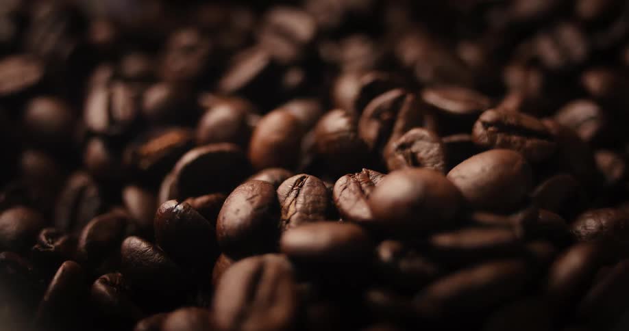 A very close view of a pile of freshly roasted dark brown coffee beans in a dimly lit atmospheric setting