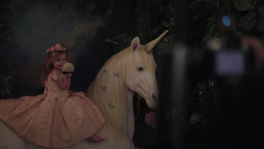 Girl wearing a light dress sitting on a decorative unicorn in a photography studio