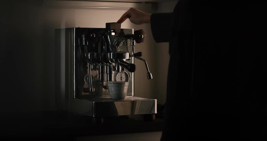 The person is standing in front of a coffee marker making coffee