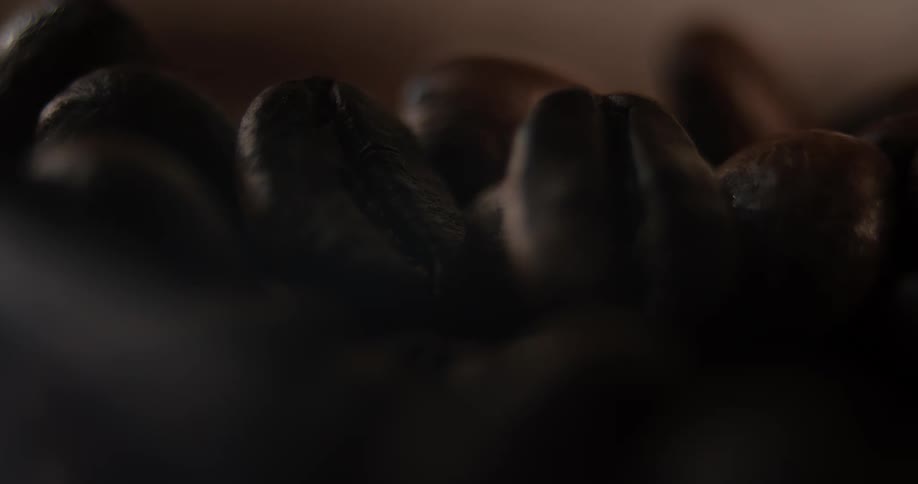 A close view shows a scattering of dark brown roasted coffee beans filling the frame under dim dramatic lighting