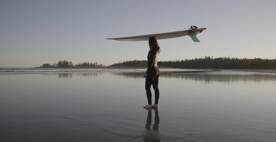 A woman balances a surfboard on her head while she stands on a beach