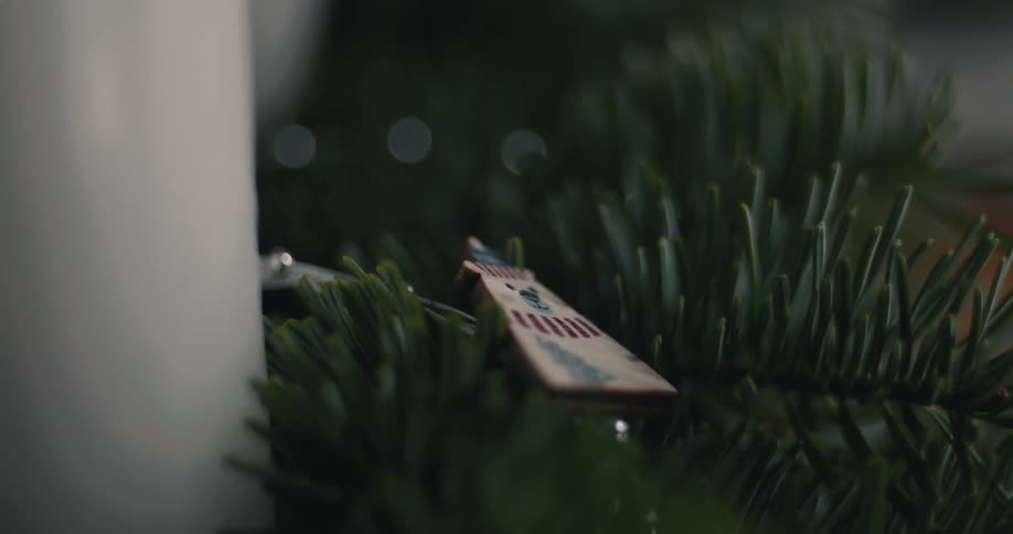 Christmas ornament shaped like a little house with striped roof hanging on pine branch