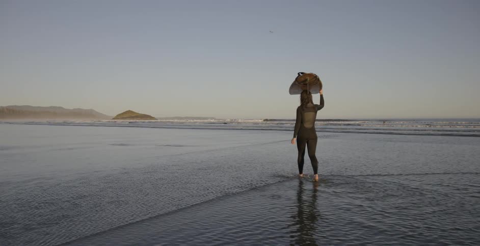 A woman walking in the water on the beach carrying a surfboard on her head