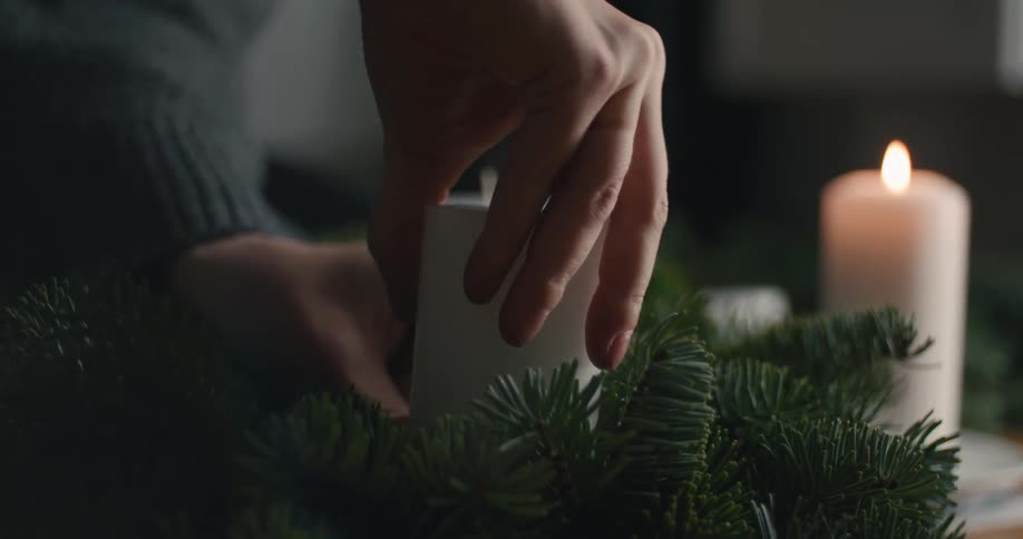 Male hands adjusting a candle over a branch of a pine tree as decoration over a table indoors