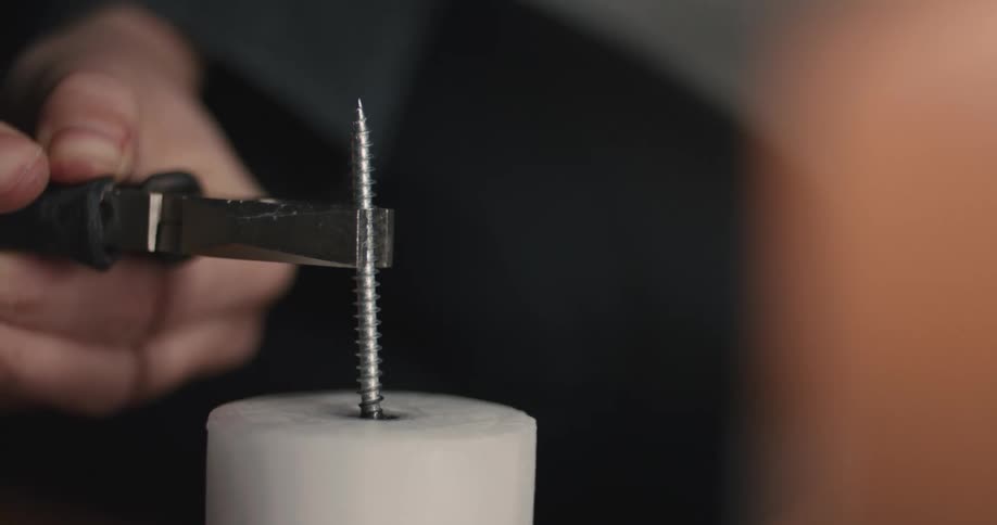 Hand holding pliers while adjusting a metal screw into a cylindrical base