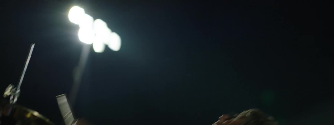 A blonde woman in a black top is captured in a closeup intensely drumming on a set with bright backlighting and her hair moving dynamically