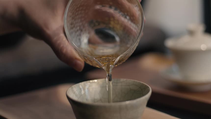 Close up of a person pouring a drink from a glass cup into a ceramic bowl