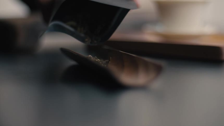 Close up of a person pouring tea leaves from a bag into a wooden half pipe in a kitchen