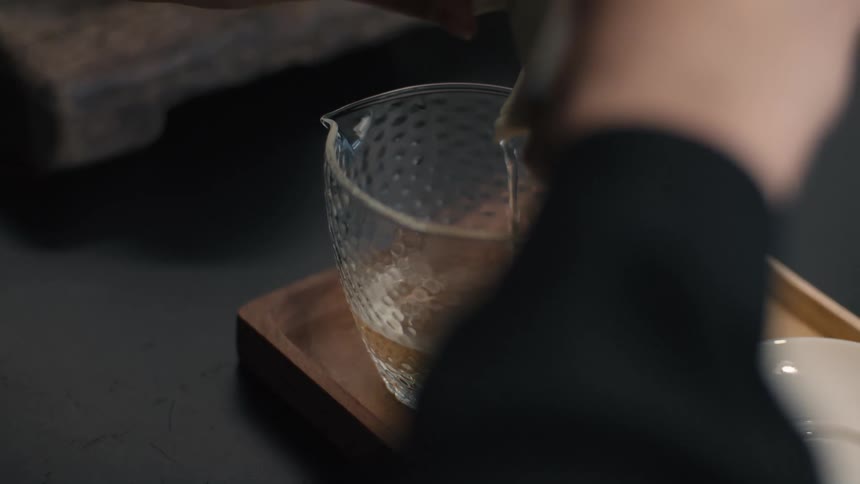 The person pours tea into the clear glass