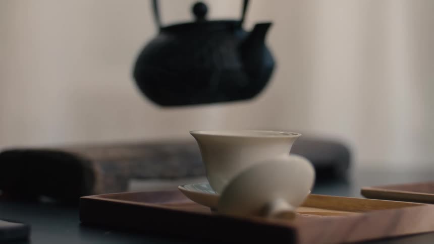 Hot water being poured from black iron teapot into white gaiwan on wooden tray
