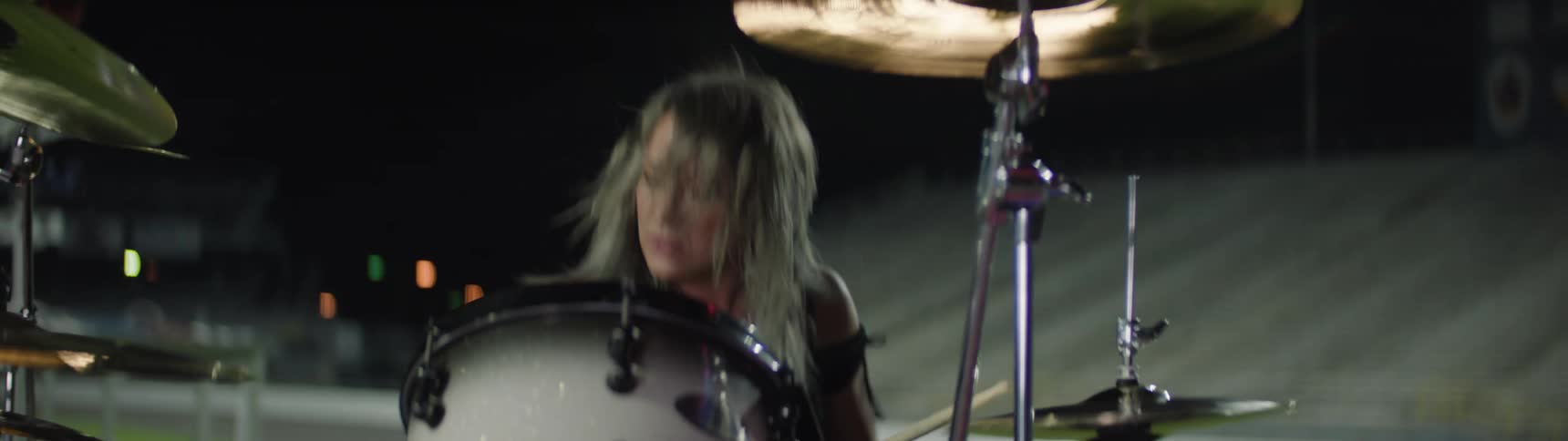 Woman holds her drumsticks and swings her arms as she hits the cymbals and plays the drums
