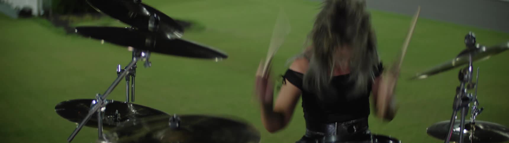 Woman holds her drumsticks and swings her arms as she hits the cymbals and plays the drums