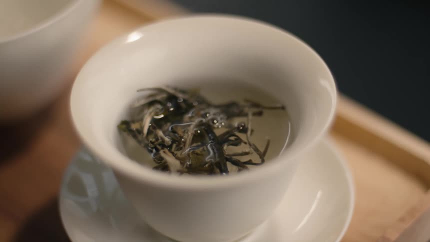 Water being poured over tea leaves on a ceramic cup over a wooden tray on a table indoors