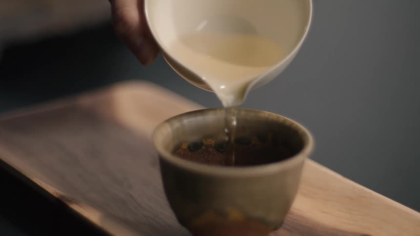 Liquid is poured from white bowl into ceramic cup on wooden tray