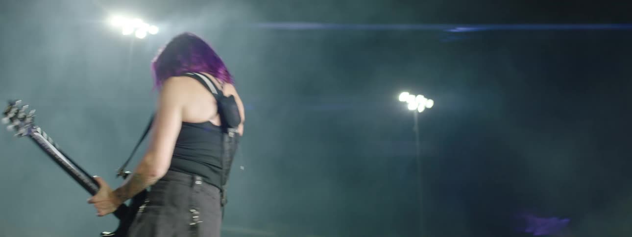 A female guitarist performing on an outdoor stage at a night concert