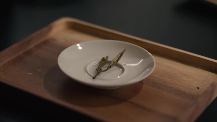 Dried leaves rest in white dish on wooden tray in simple arrangement