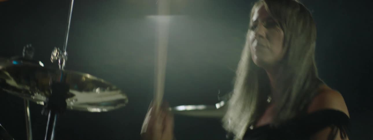 Woman holds her drumsticks as she plays the drums at a concert