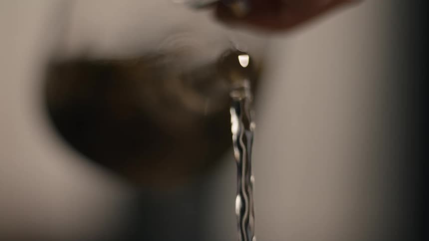 Person pours hot liquid through a spout into a cup
