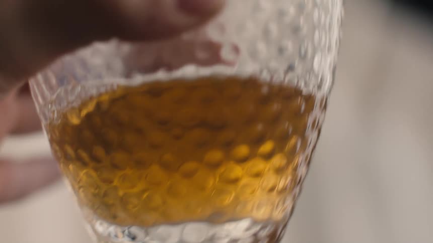 Textured glass containing brownish liquid on dark surface