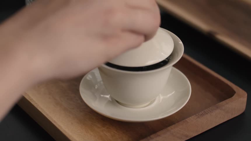 Human hands covering a cup of tea with a lid over a wodden tray on a table indoors