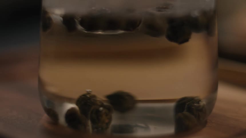 Dark round objects float in clear liquid inside glass container on wooden surface