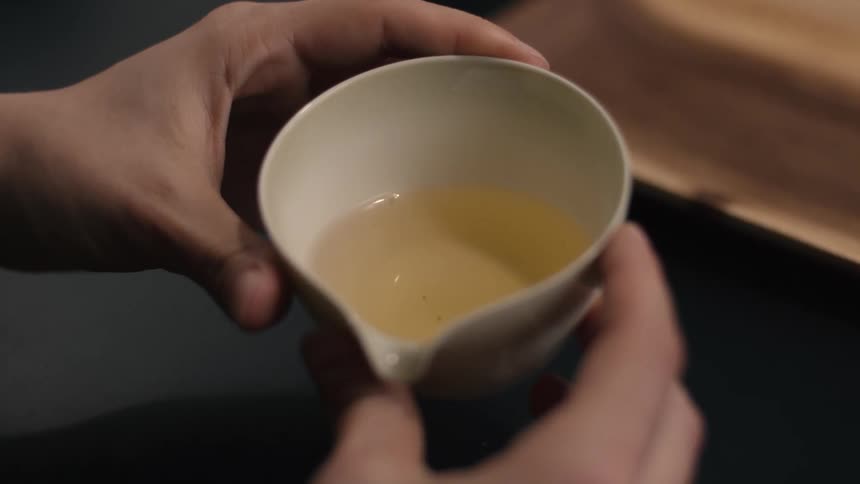 Hands hold white spouted bowl with yellowish liquid over blurred wooden surface