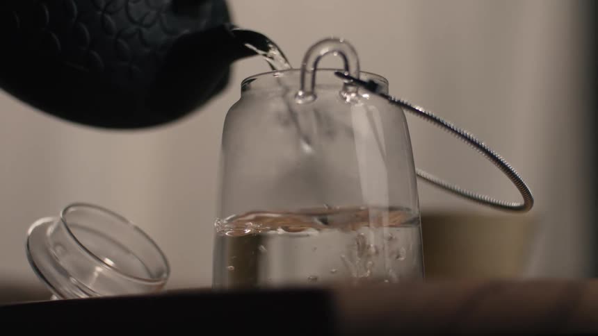 A person pours water from a dark kettle into a clear glass jar
