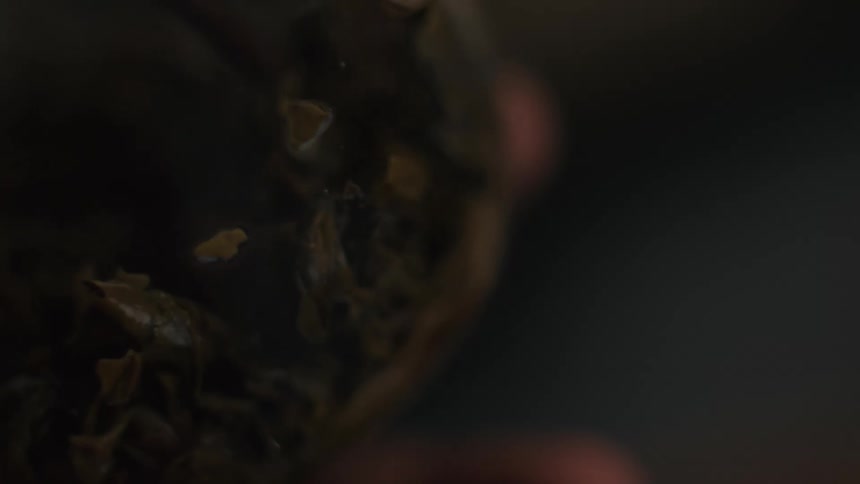 A close view of dried tea leaves or herbs inside a jar being held in the palm of a hand under dark low lighting