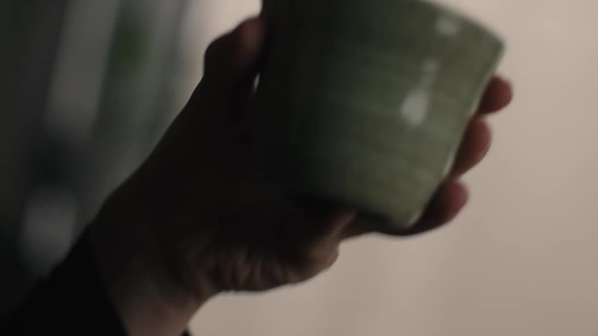 A person lifts a rustic ceramic cup from a wooden tray and brings it to their lips to take a sip