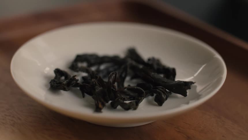 Dark twisted dried leaves in white ceramic dish on wooden surface