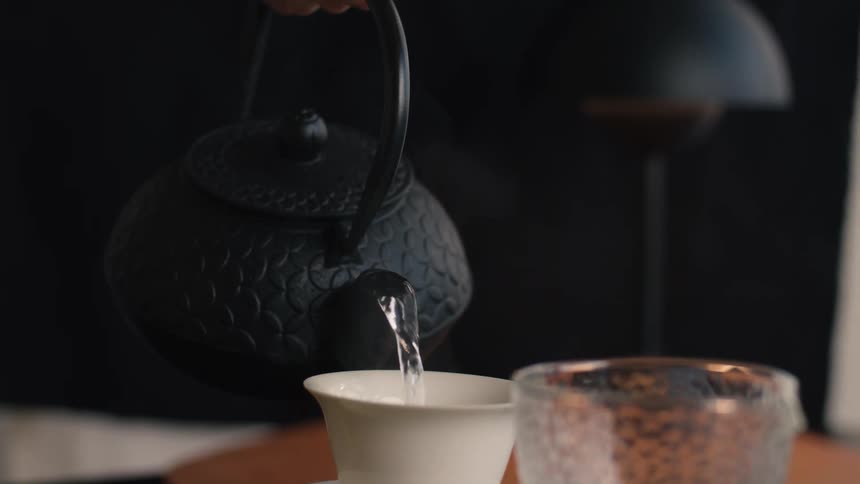 A woman pours tea from a kettle into a cup then sets the kettle aside afterward