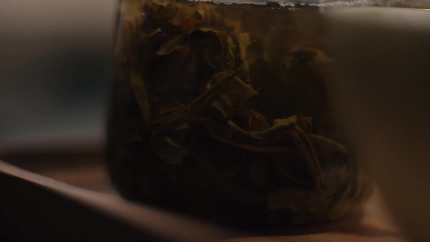 A closeup shot shows a glass vessel likely a teapot or beaker containing dark green tea leaves steeping in water the video ends as the vessel is tilted to pour with a slight shift in focus