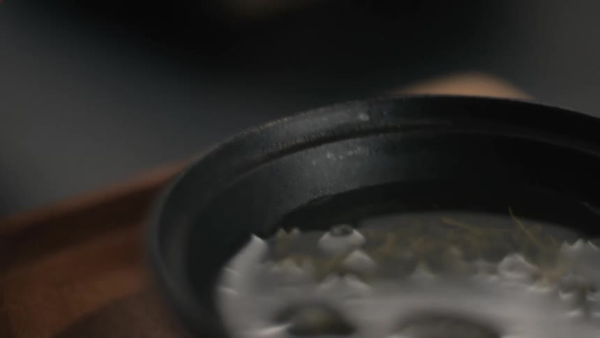 Human hands pouring water over leaves on a ceramic bowl and then covering it with a lid indoors