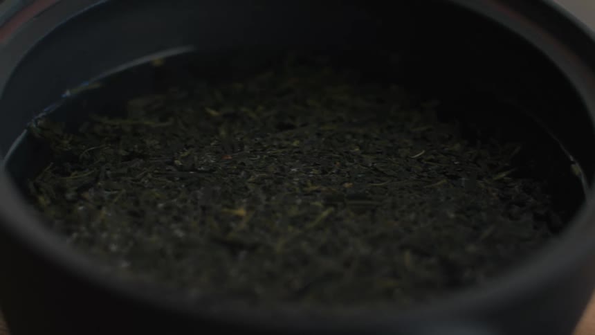 Dark leaves immersed in liquid rest inside black pot on wooden surface