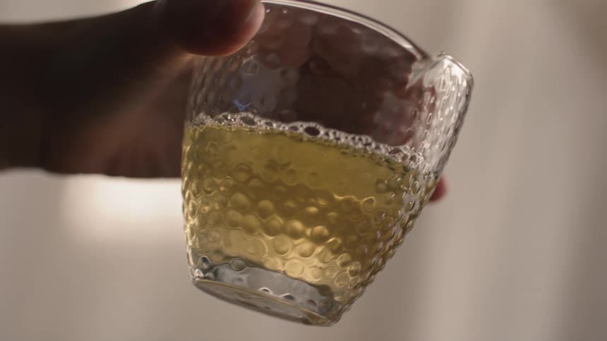 Close up of a person holding a glass cup containing a yellowish drink
