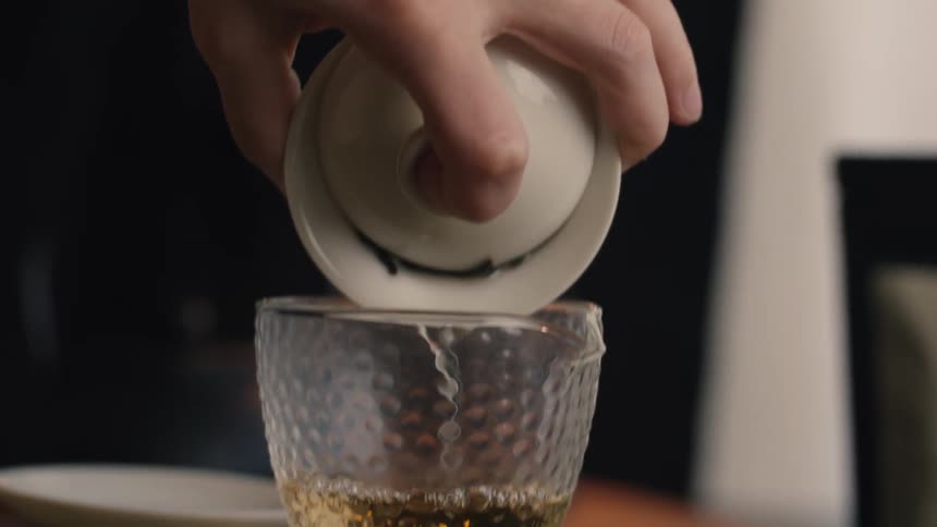 Clear liquid being poured from white ceramic lid into textured glass container with blurred background